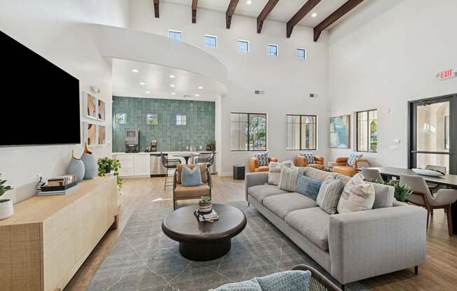 A modern living room with a grey sofa, a wooden coffee table, and a large flat-screen TV mounted on the wall.