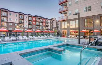 A swimming pool surrounded by lounge chairs and umbrellas in front of apartment buildings.