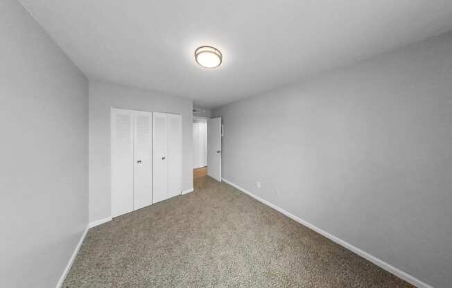 a bedroom with white walls and carpet and white closet doors