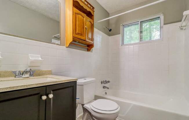 A white toilet sits in a bathroom with a white tub and a window.