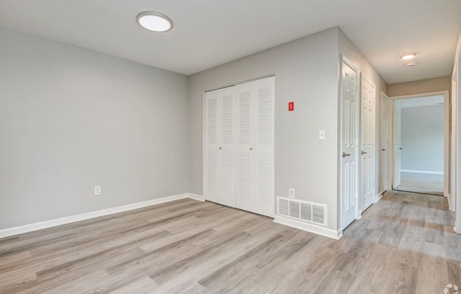 an empty room with a door to a closet and a hallway with wood flooring