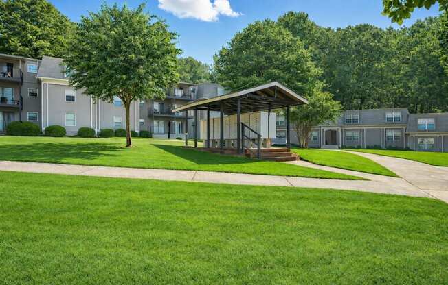 A grassy area with a pavilion and apartment buildings in the background.