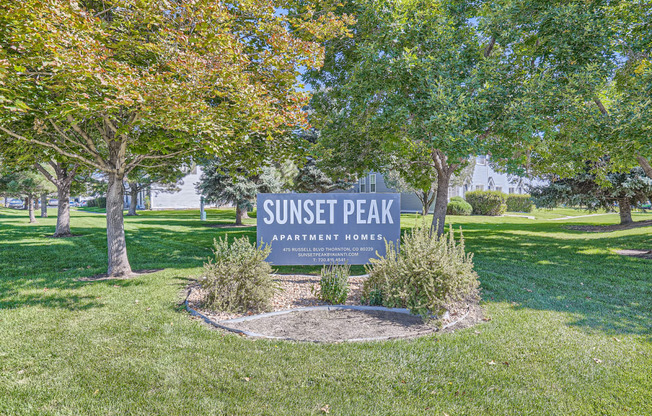 a park with trees and grass and a sign that says sunset peak apartments
