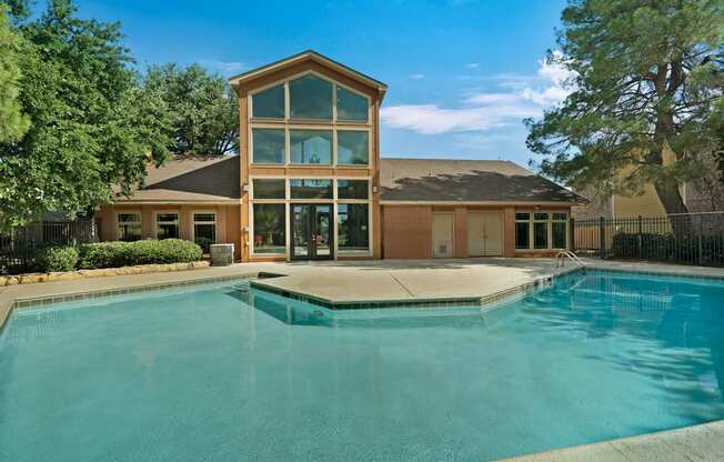 A refreshing outdoor swimming pool here at The Bradford with clear blue water, wide pool decking, and a modern clubhouse backdrop. A landscaped setting with mature trees and open sky creates a relaxing, resort-style atmosphere for residents.