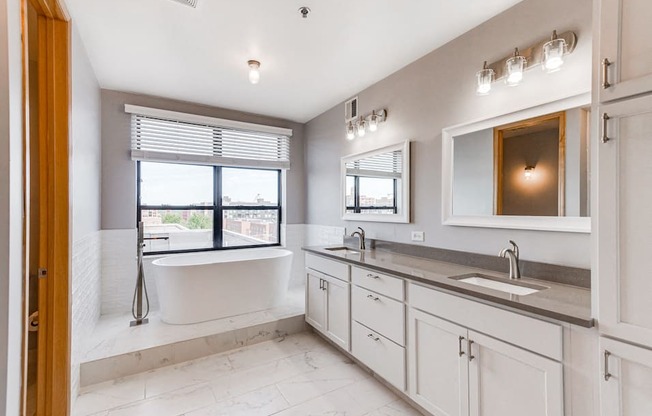 Bathroom with dual sinks and a bathtub next to the window