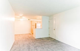 an empty living room with a kitchen in the background