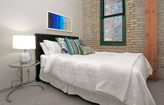 Side view of spacious bedroom with exposed brick wall and wood beam near window.