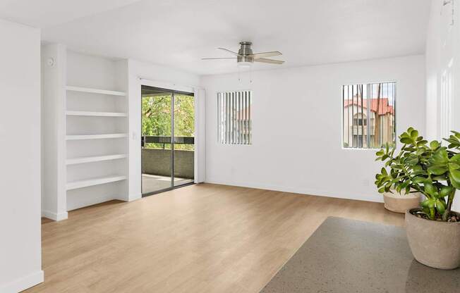 A room with a sliding glass door leading to a balcony, a ceiling fan, and a rug on the floor.