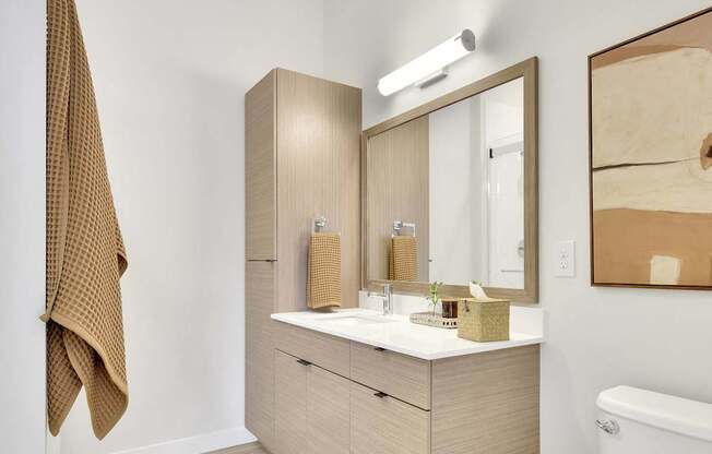 A white toilet sits in a bathroom with a wooden vanity and a mirror.