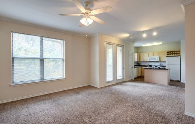 an empty living room with a ceiling fan and a kitchen