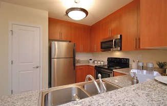 Kitchen with stainless steel appliances; granite countertops; open to living space