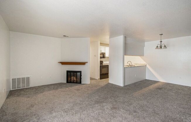 an empty living room with a fireplace and a kitchen