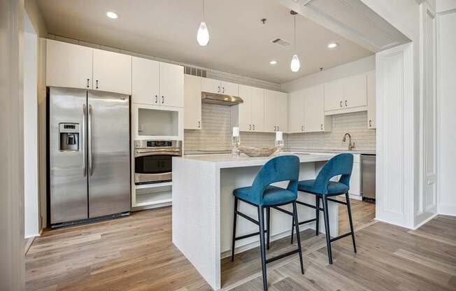 A kitchen with a refrigerator, oven, and two chairs.
