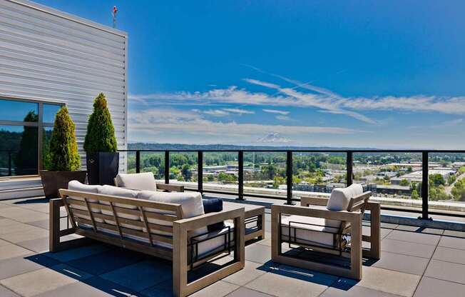 Two wooden chairs and a sofa on a patio overlooking a cityscape.