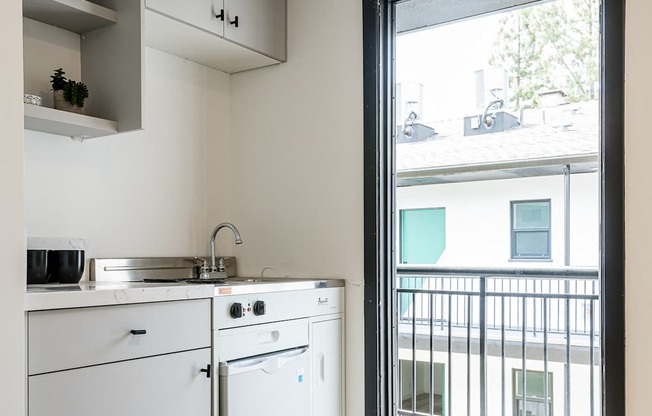 A modern kitchen with white appliances and a window overlooking a balcony.