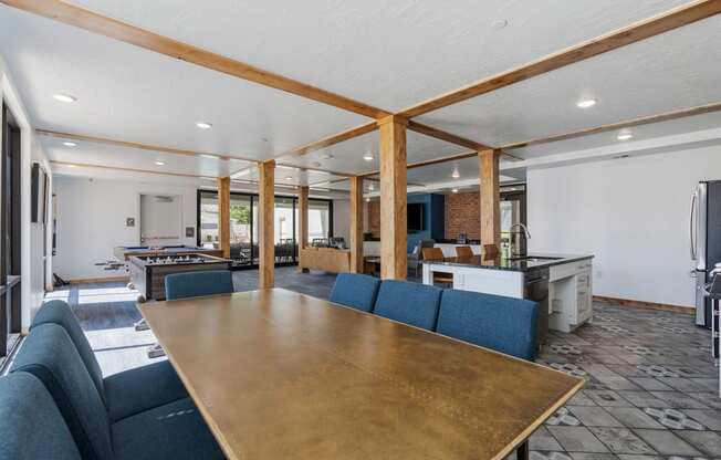 the gathering room has a large table with blue chairs and a kitchen and dining area