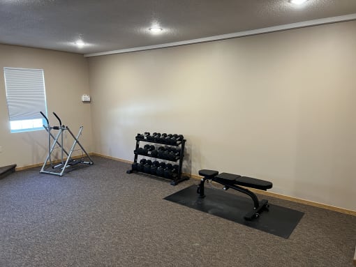 a small exercise room with weights and a bench at Bluemont Village Apartments, Fargo, 58104