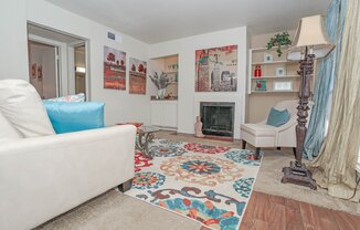 Large model living room with a white couch and a colorful rug facing a fireplace at Laurel Parc apartments in Shreveport, LA.