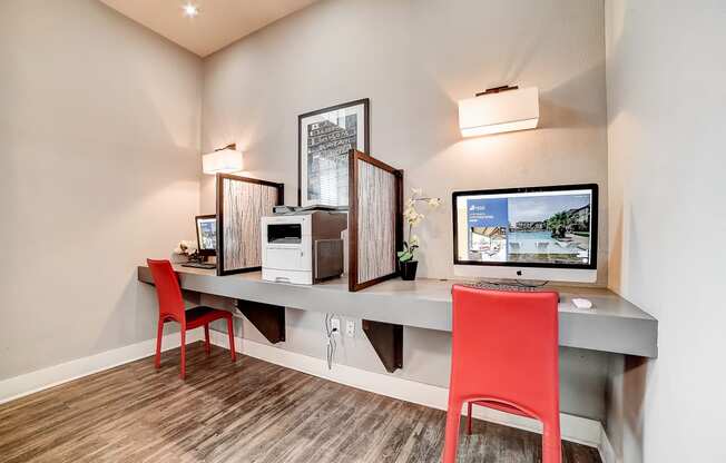 a desk with two computer monitors and two red chairs