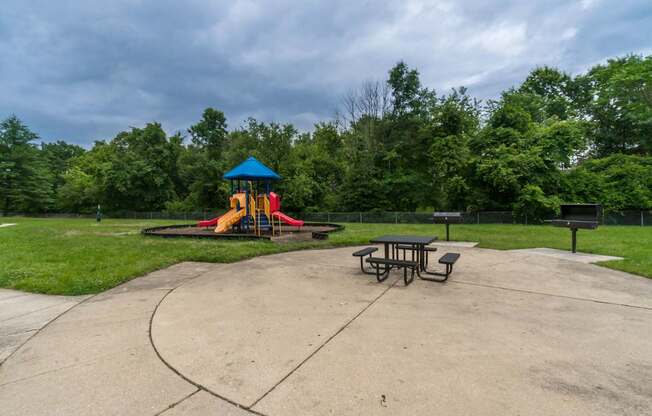 A playground with a blue and yellow slide, picnic tables, and a concrete area.