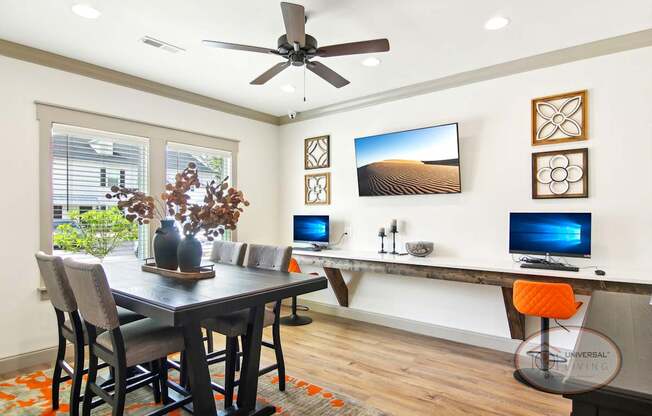 The business center with computers and bar stool seating, a table and chairs, and a flat screen TV.