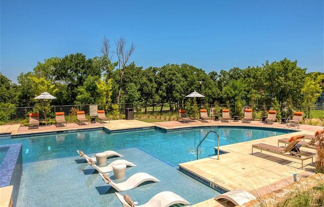 Apartments in Grapevine TX - Large Swimming Pool Surrounded By Lounge Chairs and Outdoor Umbrellas