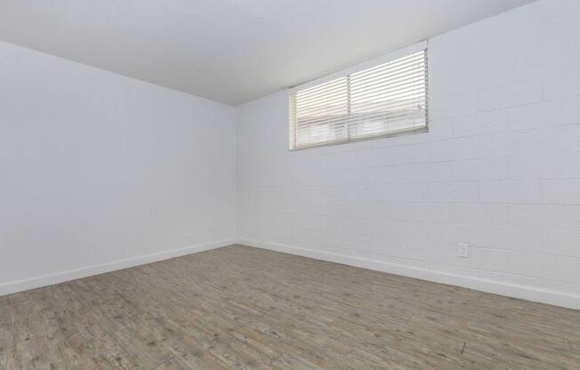 A room with wooden flooring and a window with blinds.