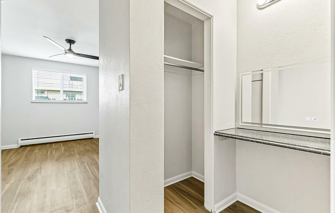 Bright and airy apartment corner featuring an elegant closet space with shelving, sleek vanity area, and a modern ceiling fan above exquisite wood flooring.