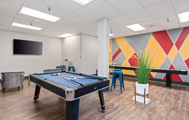 A pool table in a room with a TV mounted on the wall.