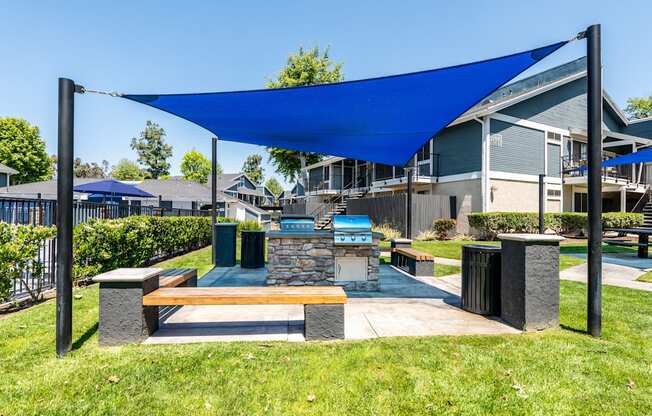 A blue shade structure is over a bench in a grassy area.