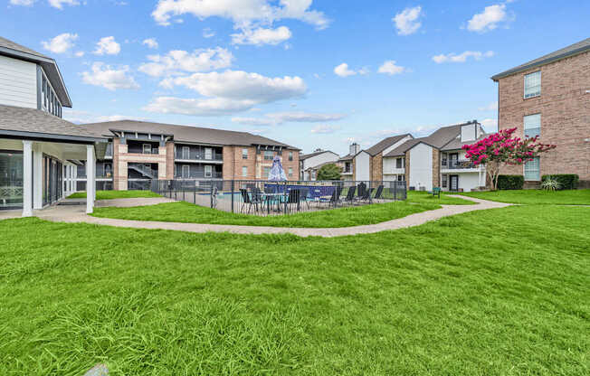 A grassy area in front of apartment buildings with a pink flowering bush.