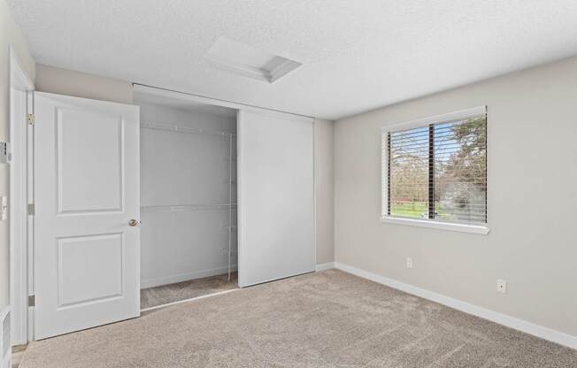 A room with a white door, a window with blinds, and a carpeted floor.