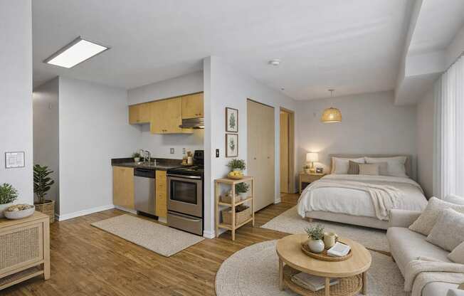 A modern kitchen with wooden cabinets and a white countertop is adjacent to a cozy bedroom with a large bed and a nightstand.