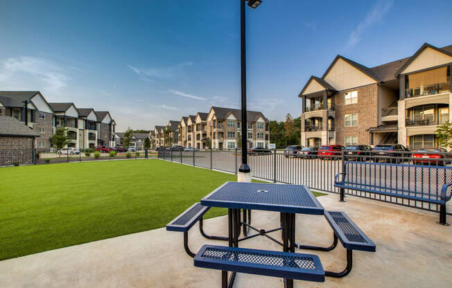 a picnic table with a view of a grassy area and apartment buildings in the background