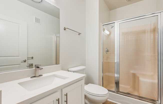 A white bathroom with a sink, toilet, and shower.