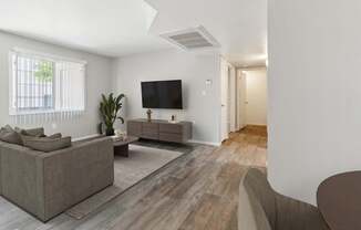 A living room with a grey couch, a brown armchair, a wooden floor, and a flat-screen TV mounted on the wall.