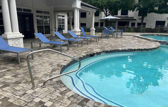 a resort style pool with blue chairs and a building in the background