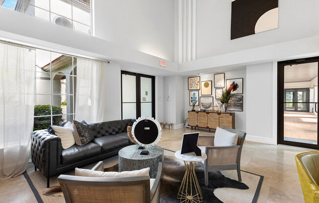 A black leather couch sits in a brightly lit room with a yellow chair and a table with a fan.