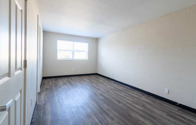 the living room of an empty apartment with wood flooring and a window