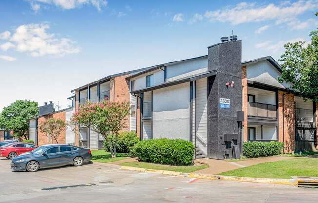 A grey car is parked in front of a building with a blue sign on it.