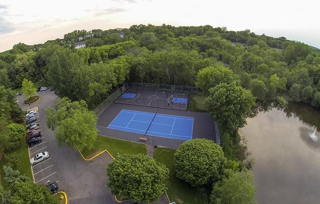 Aerial view of a blue basketball and tennis court surrouned by trees