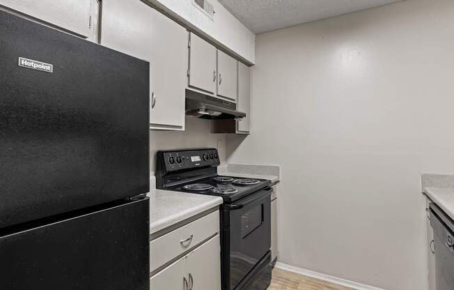 A black refrigerator is in a kitchen with white cabinets.