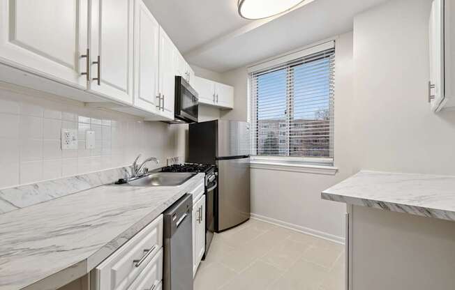 A kitchen with white cabinets, stainless steel appliances, and a marble countertop.