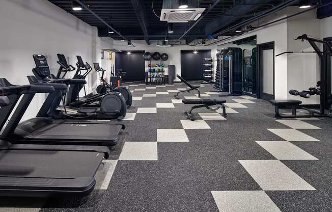 A gym with treadmills, weights, and a checkerboard floor.