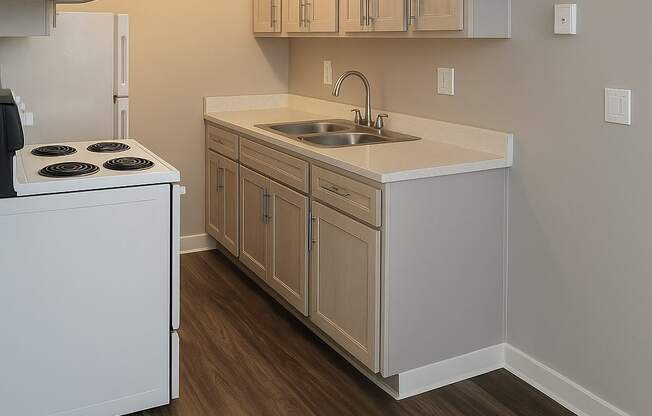 A kitchen with a white stove top oven and a white sink with a white counter top.