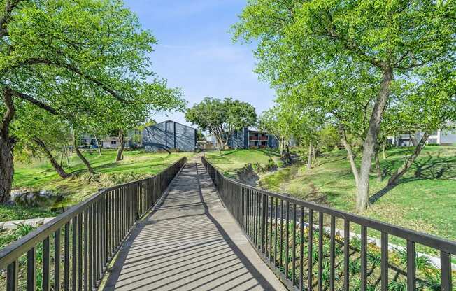 A wooden walkway with metal railings leads through a lush green park.