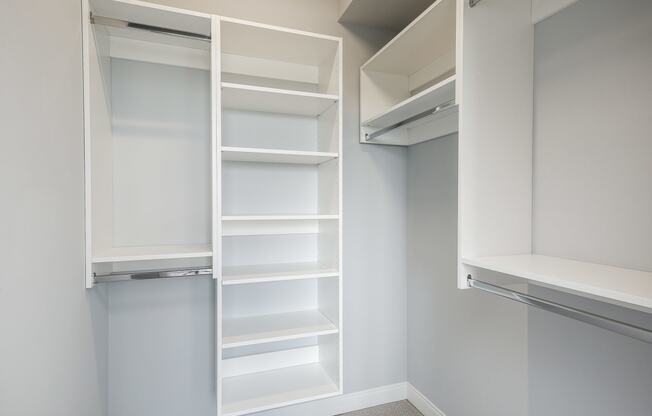 a walk in closet with white shelving and empty shelves
