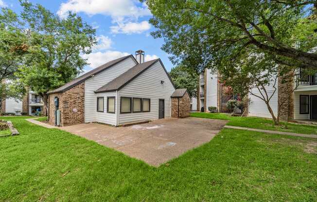 A house with a grey roof and a stone chimney is surrounded by a green lawn.