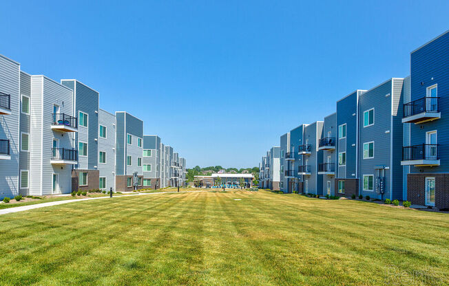 A row of modern apartment buildings with a grassy lawn in the foreground at Lofts at Fox Ridge, Raymore, MO, 64083