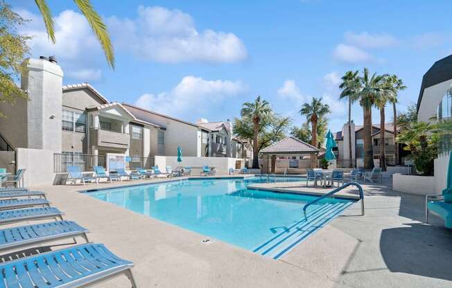A swimming pool surrounded by sun loungers and palm trees.